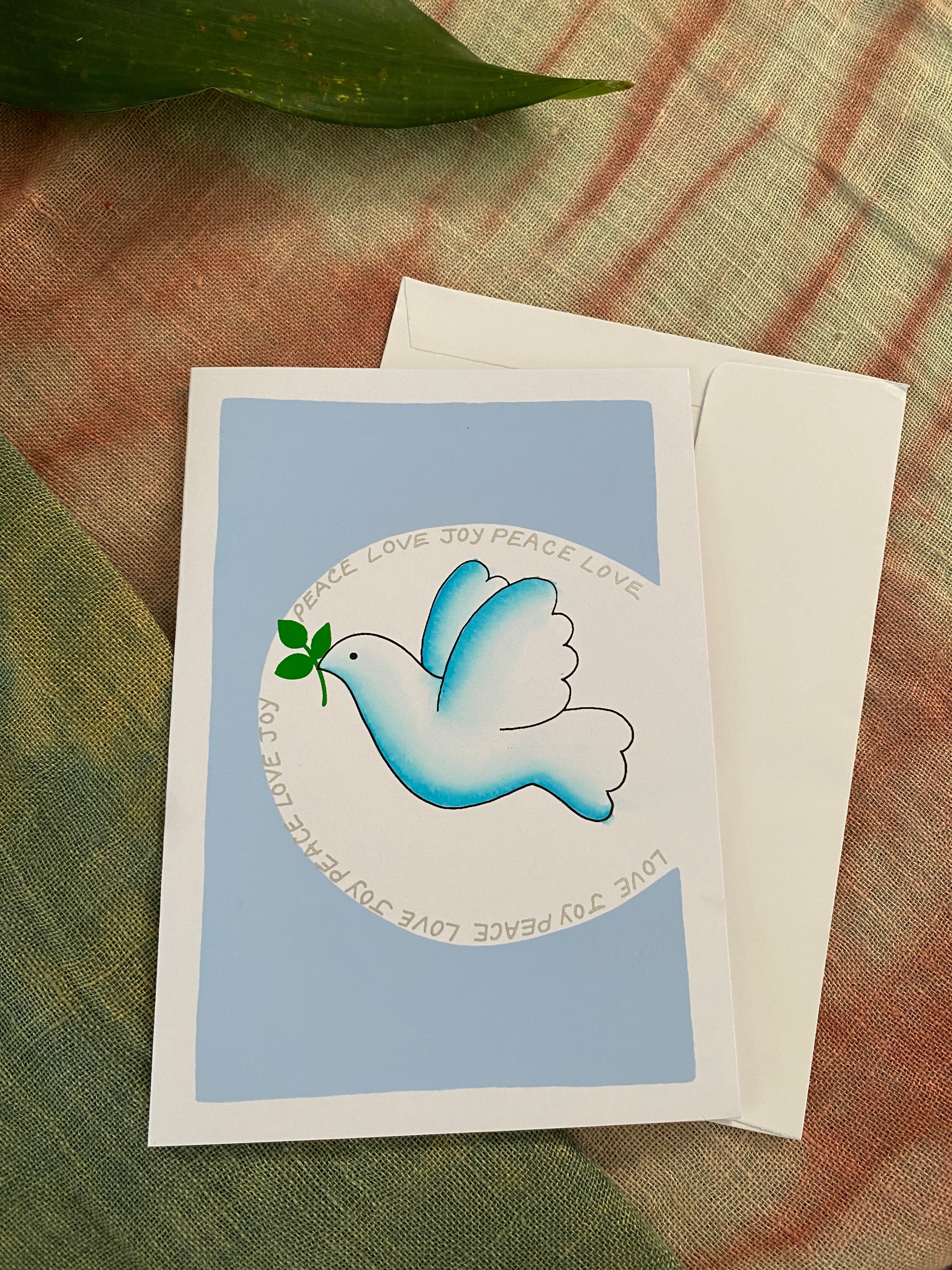 Greeting card with a dove design , with peace , love , joy written around the dove on a textured fabric background