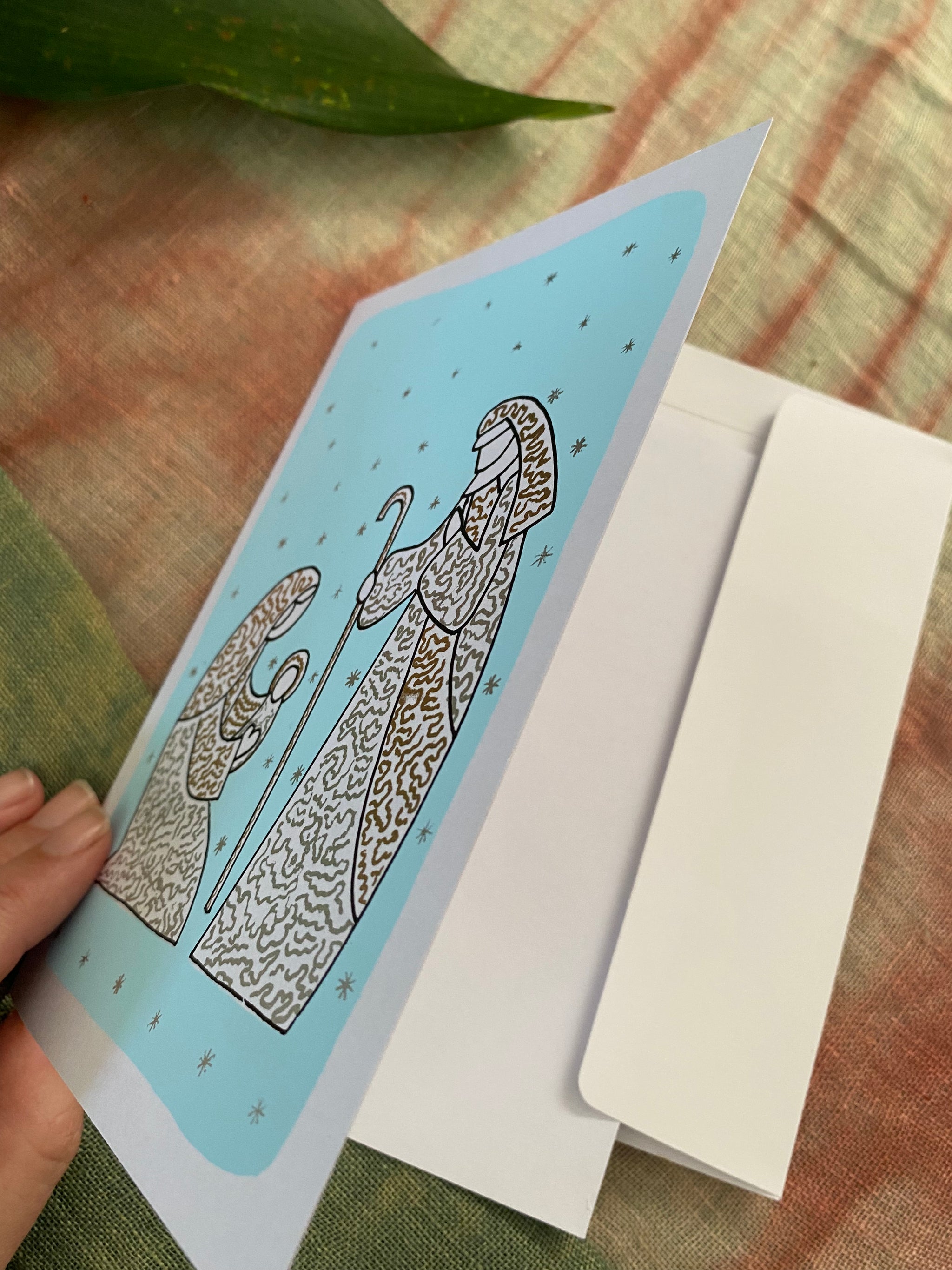 a Hand holding card open to show its blank inside. on the front of the Christmas card is the nativity .