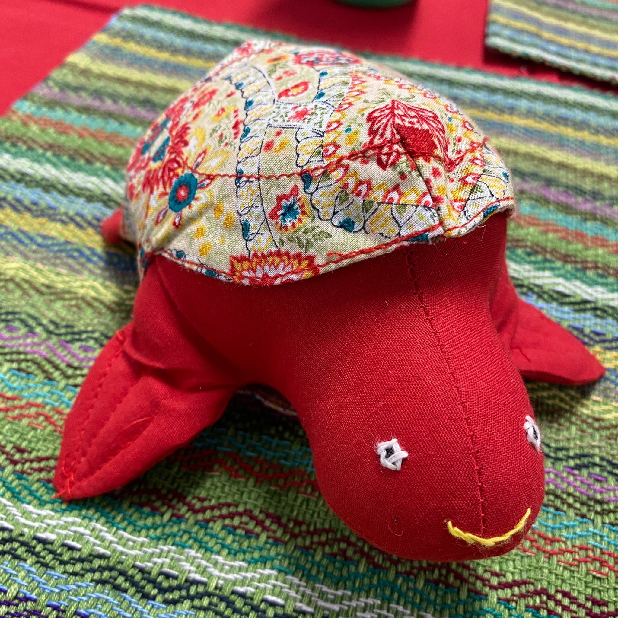 Cute red fabric turtle with a patterned fabric removable shell. Displayed on a colourful green background