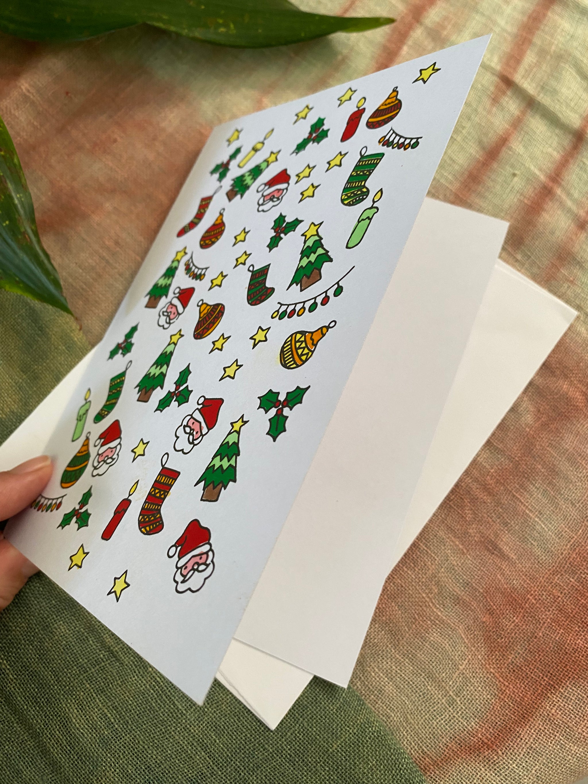 Sheet of Christmas-themed icons on a card held over a white envelope on a textured surface.