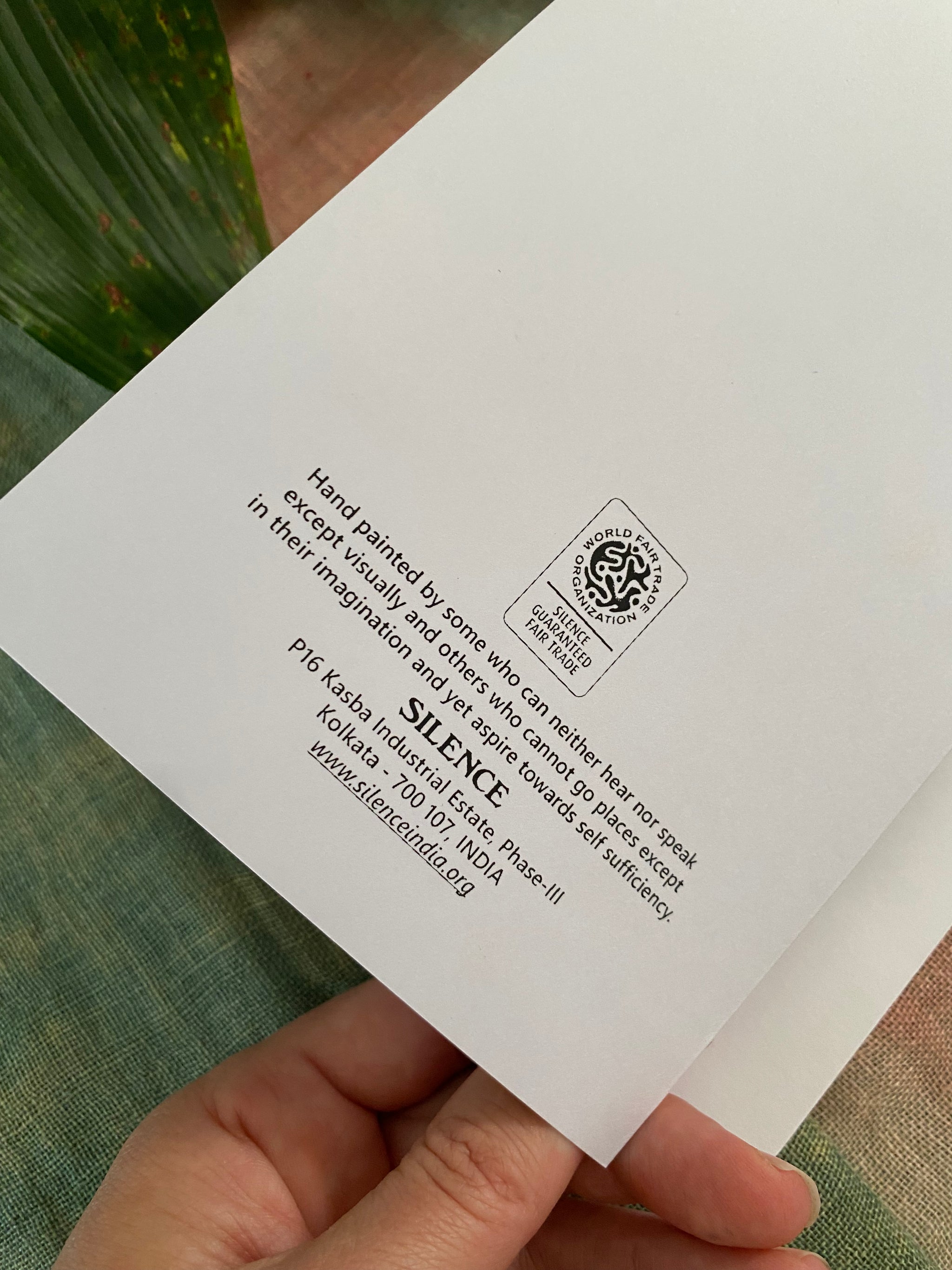Hand holding a white card with text and a WFTO logo on a textured surface