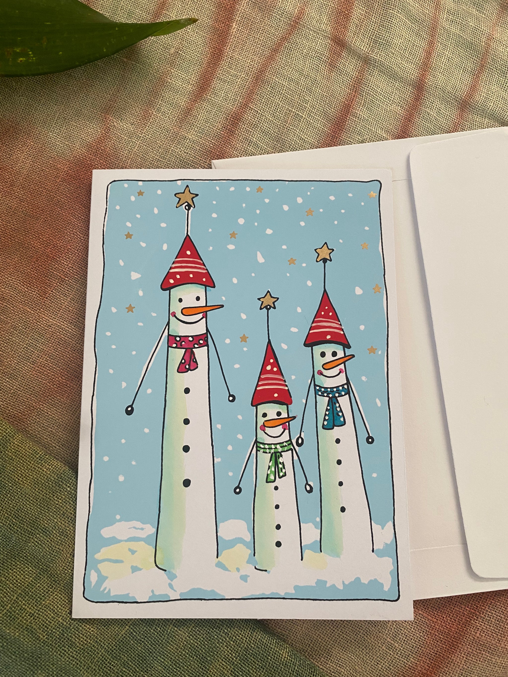 playful Christmas card featuring three tall, cheeky snow people with big smiles and fun personalities. Standing together in the snow, they look ready for Christmas mischief and joy