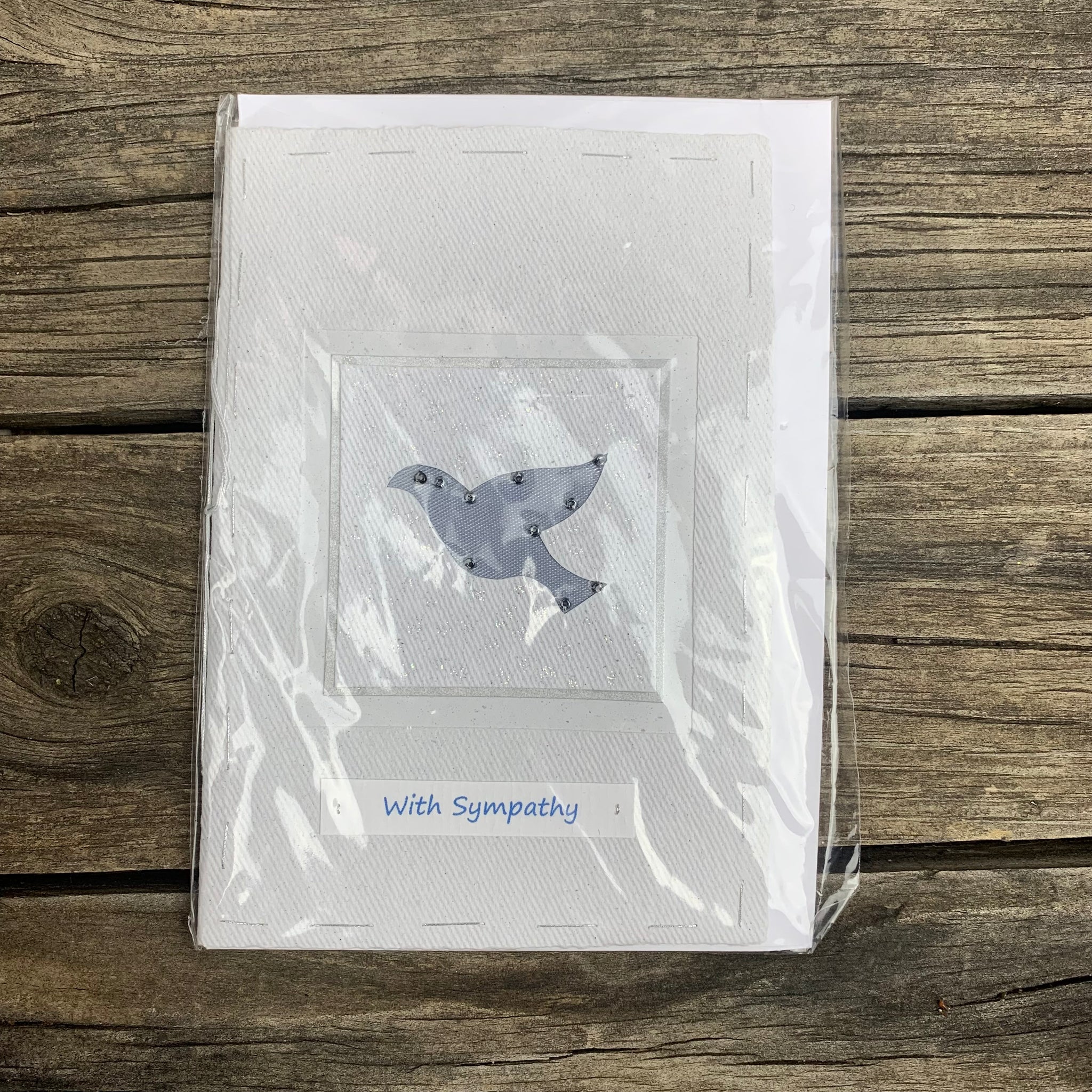 White handmade paper greeting card displaying 'With Sympathy" in baby blue cursive letters. A jewel adorned grey dove is also displayed in the centre