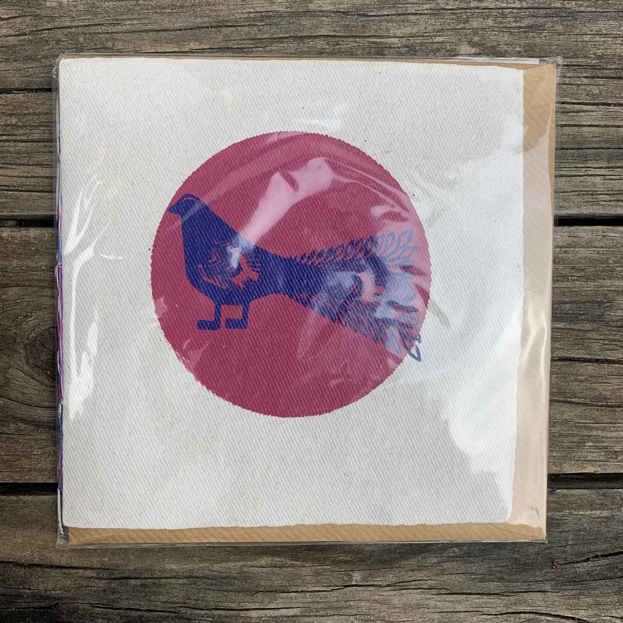 White handmade paper greeting card featuring a magenta coloured circle in the centre framing a dark blue bird design. There is no message