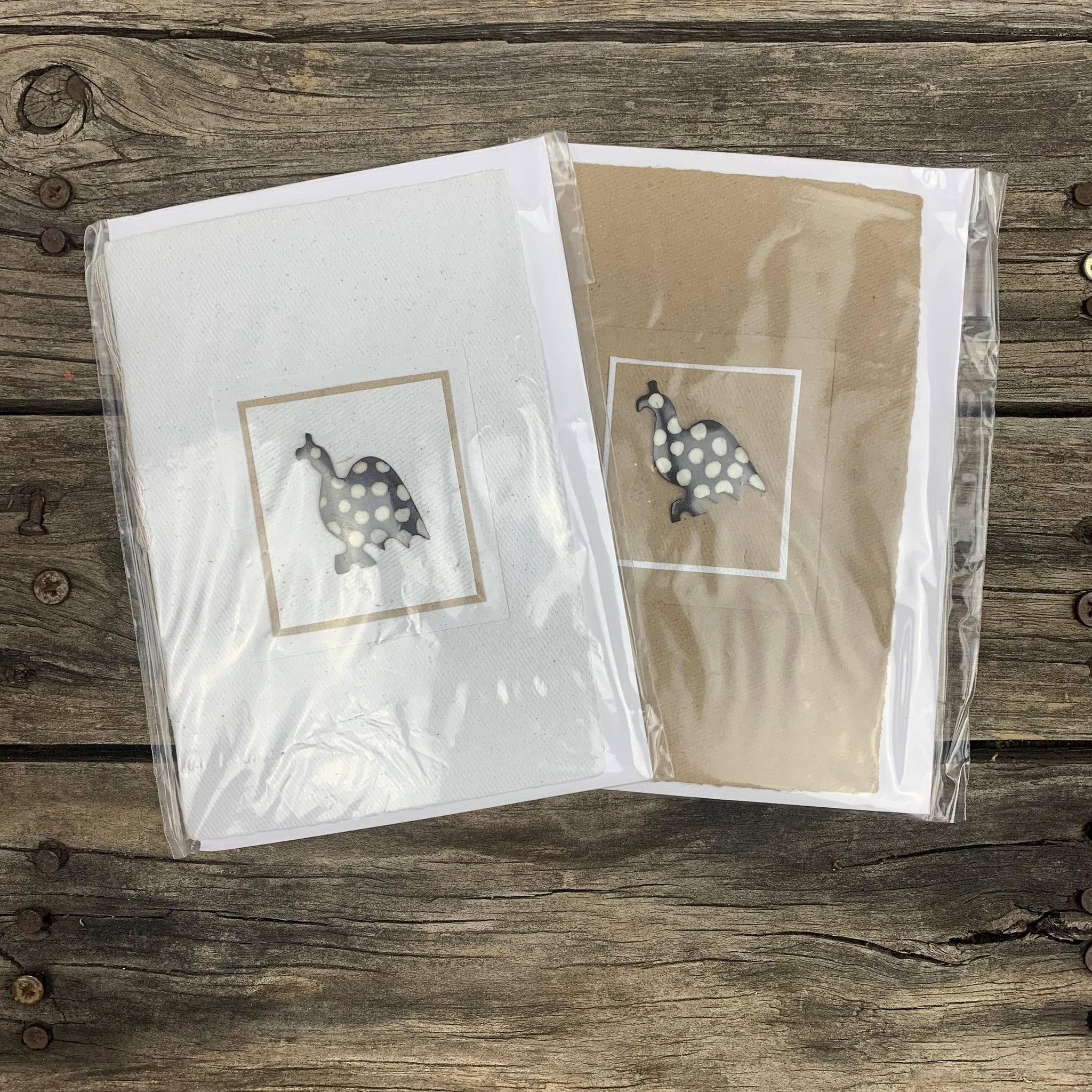 greeting card in either brown or white handmade paper. The card has a small ginea foul design in the centre, with polik dots, that protrudes from the surface. The bird is also framed by either a brown or white border. There is no message