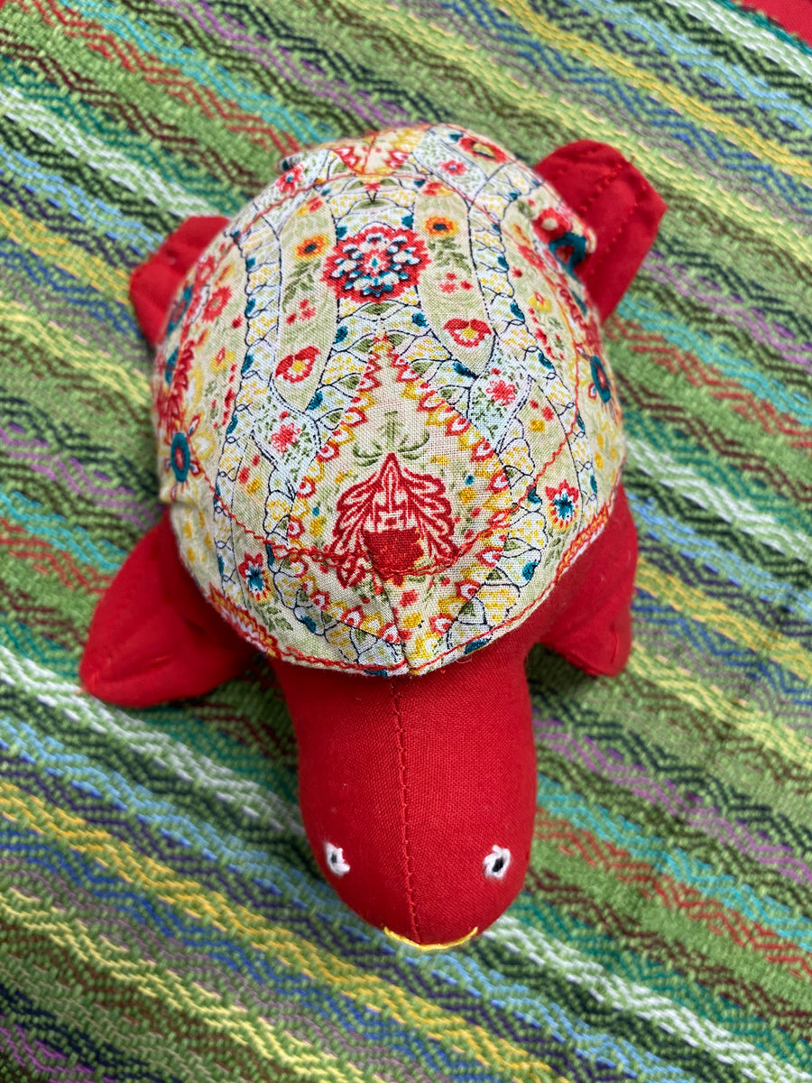 Cute red fabric turtle with a patterned fabric removable shell. Displayed on a colourful green background