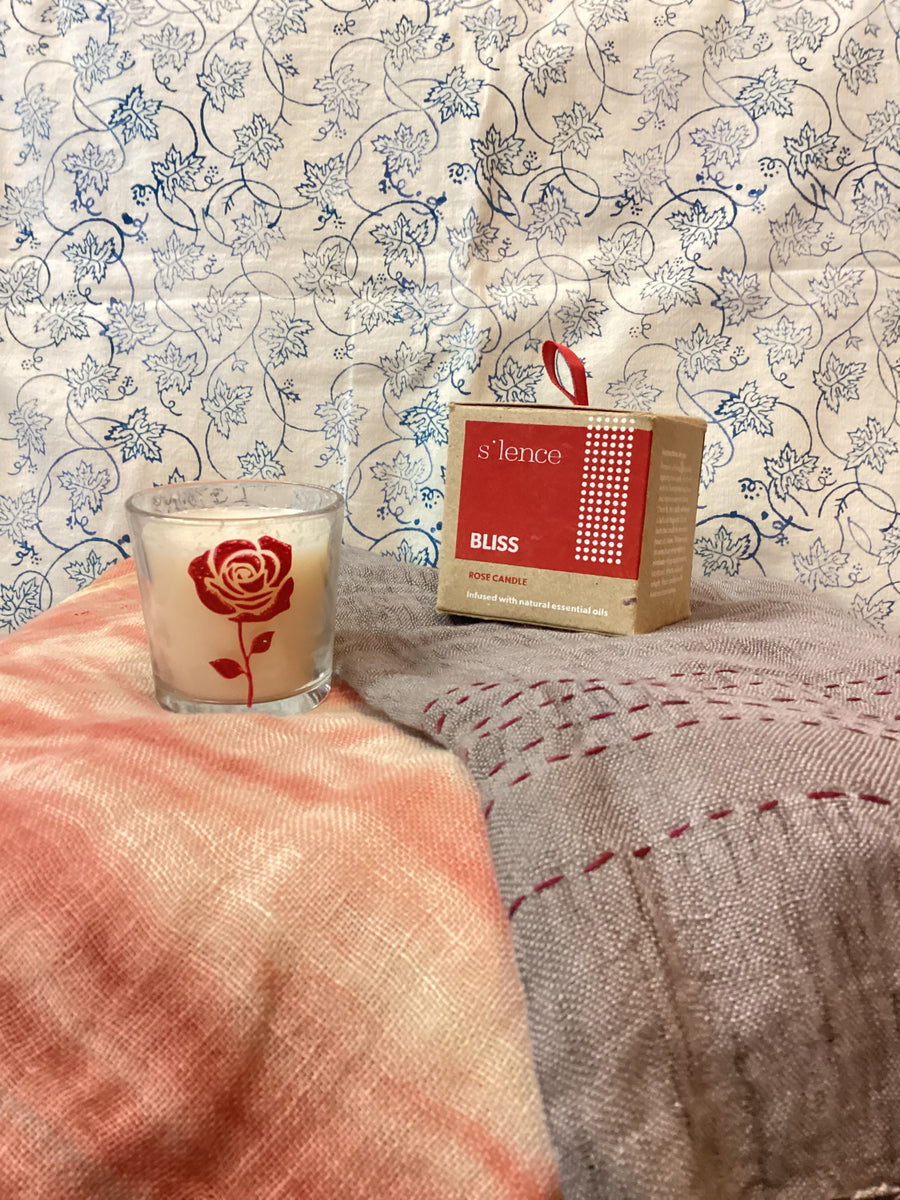 Candle with a red rose design on a textured surface with floral wallpaper in the background