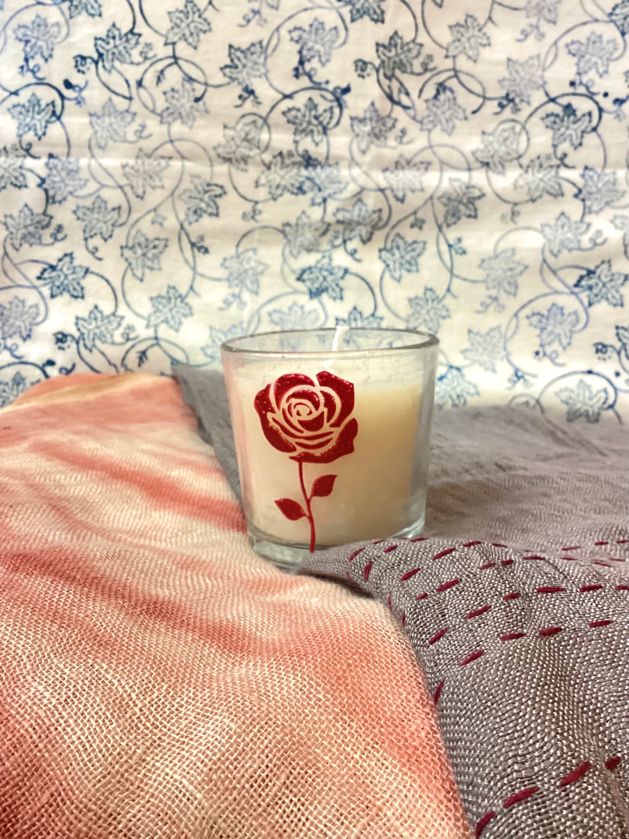 Candle with a red rose design on a textured surface with floral wallpaper in the background
