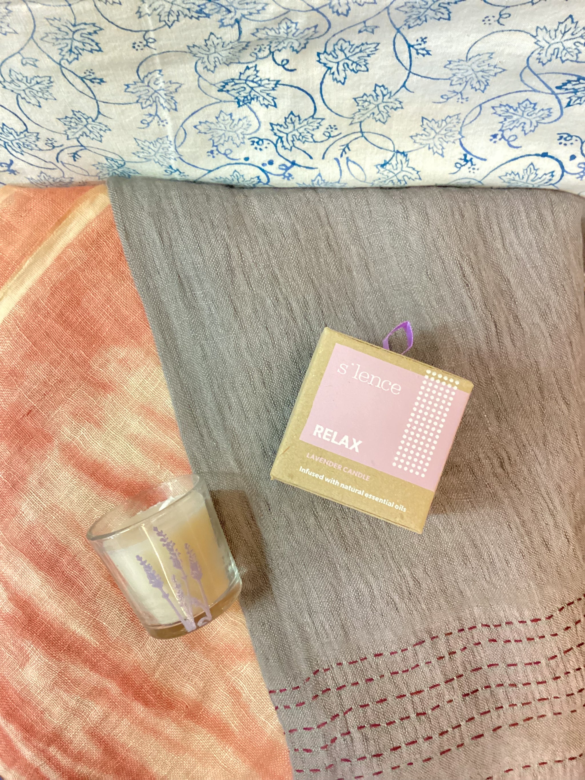Candle and packaging on a textured surface with floral patterned fabric in the background
