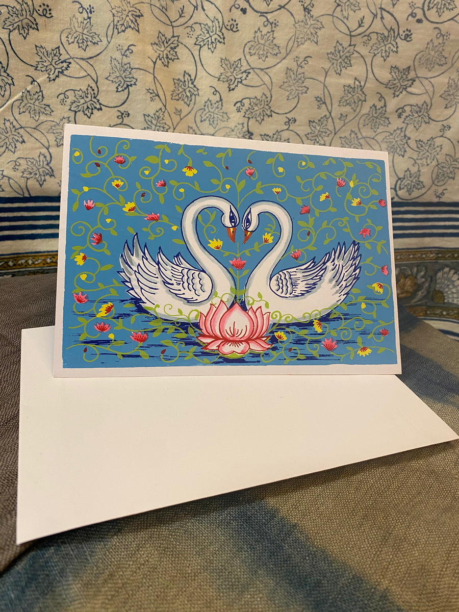 Decorative card with two swans and a lotus flower on a blue background, featuring floral patterns.