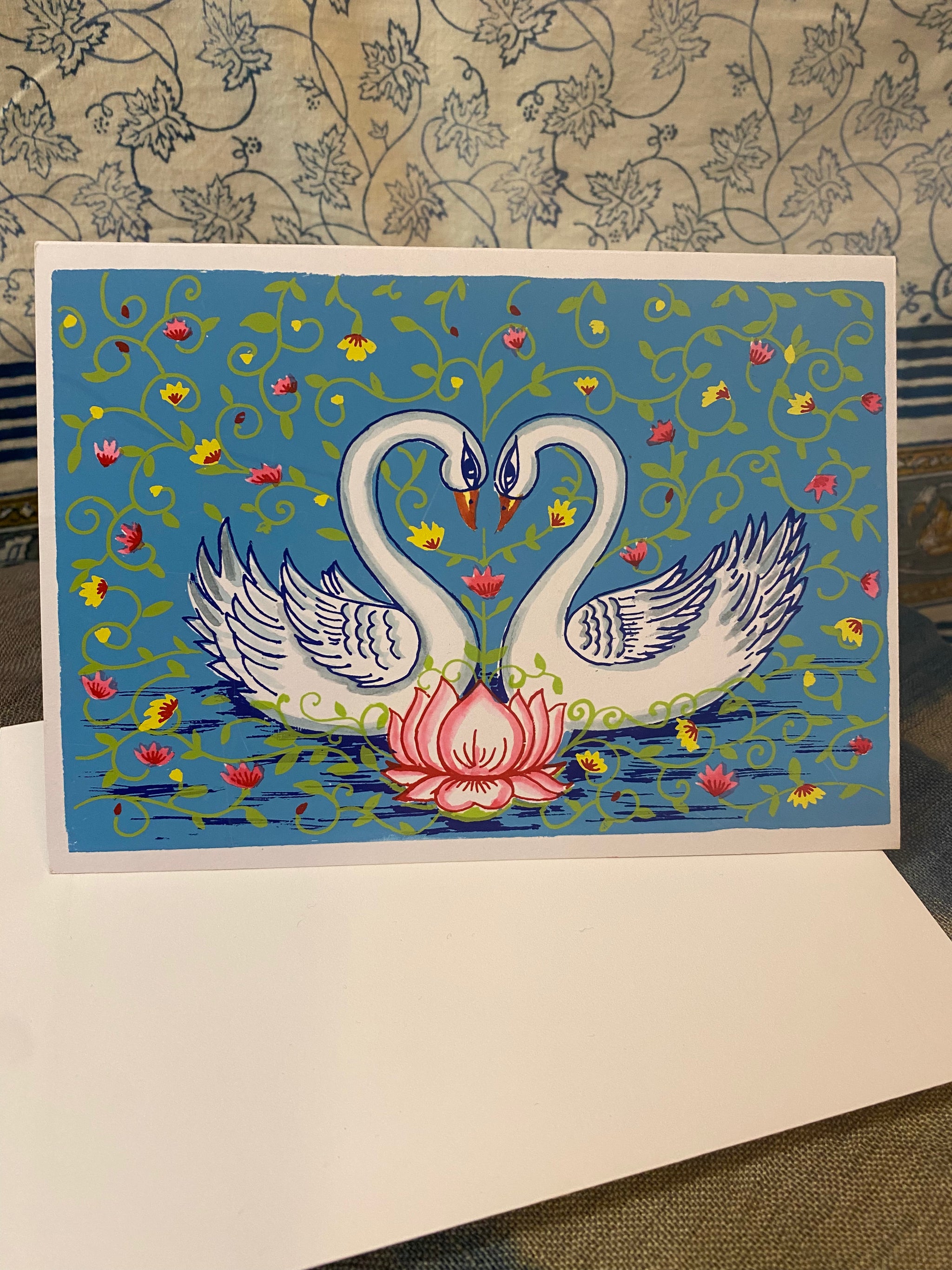 Decorative card with two swans and a lotus flower on a blue background, featuring floral patterns.