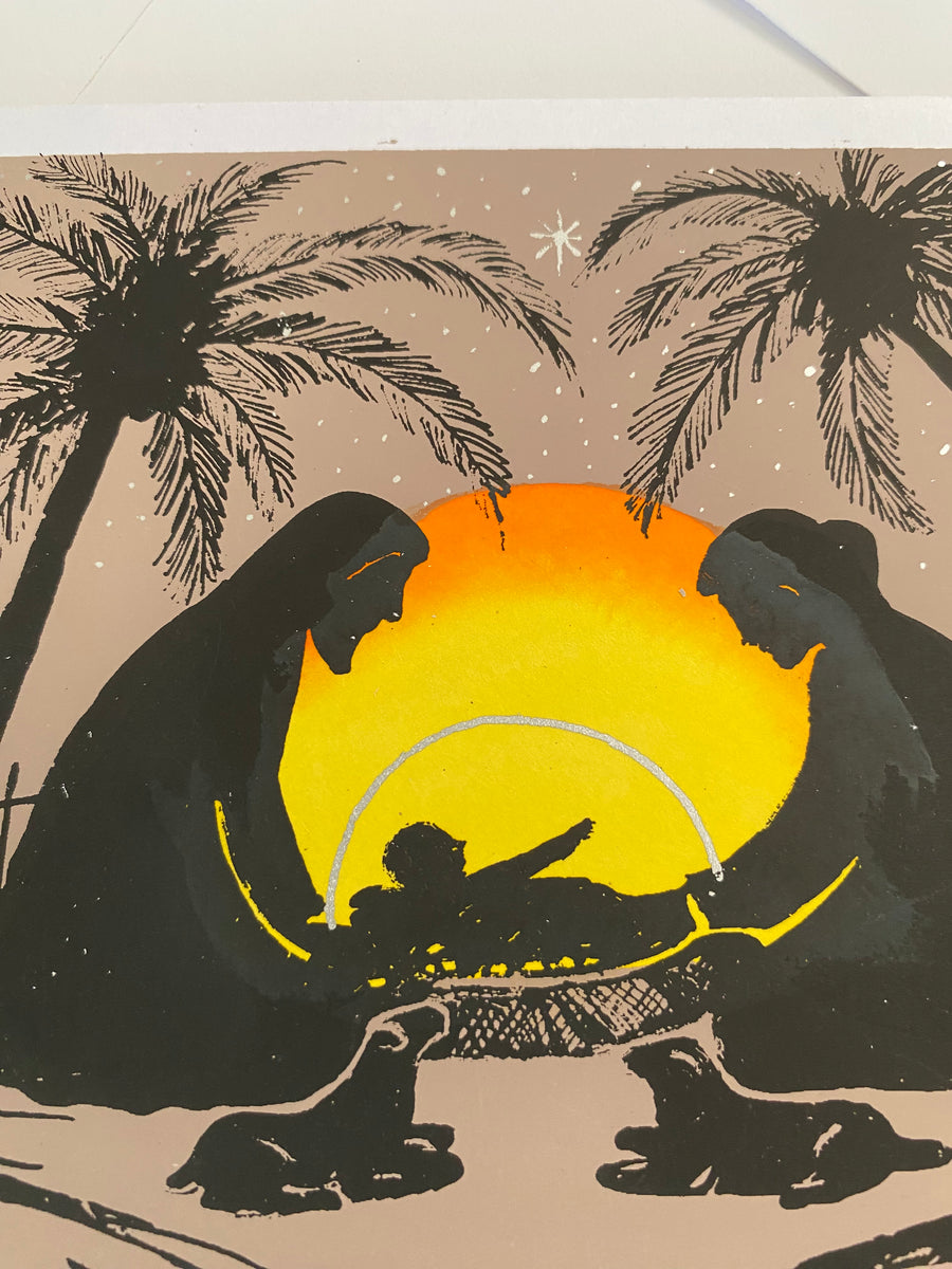 Christmas card landscape-format card showing Mary, Joseph and baby Jesus in silhouette beneath a glowing sunset. Palm trees, sheep and the setting sun frame the holy family, 