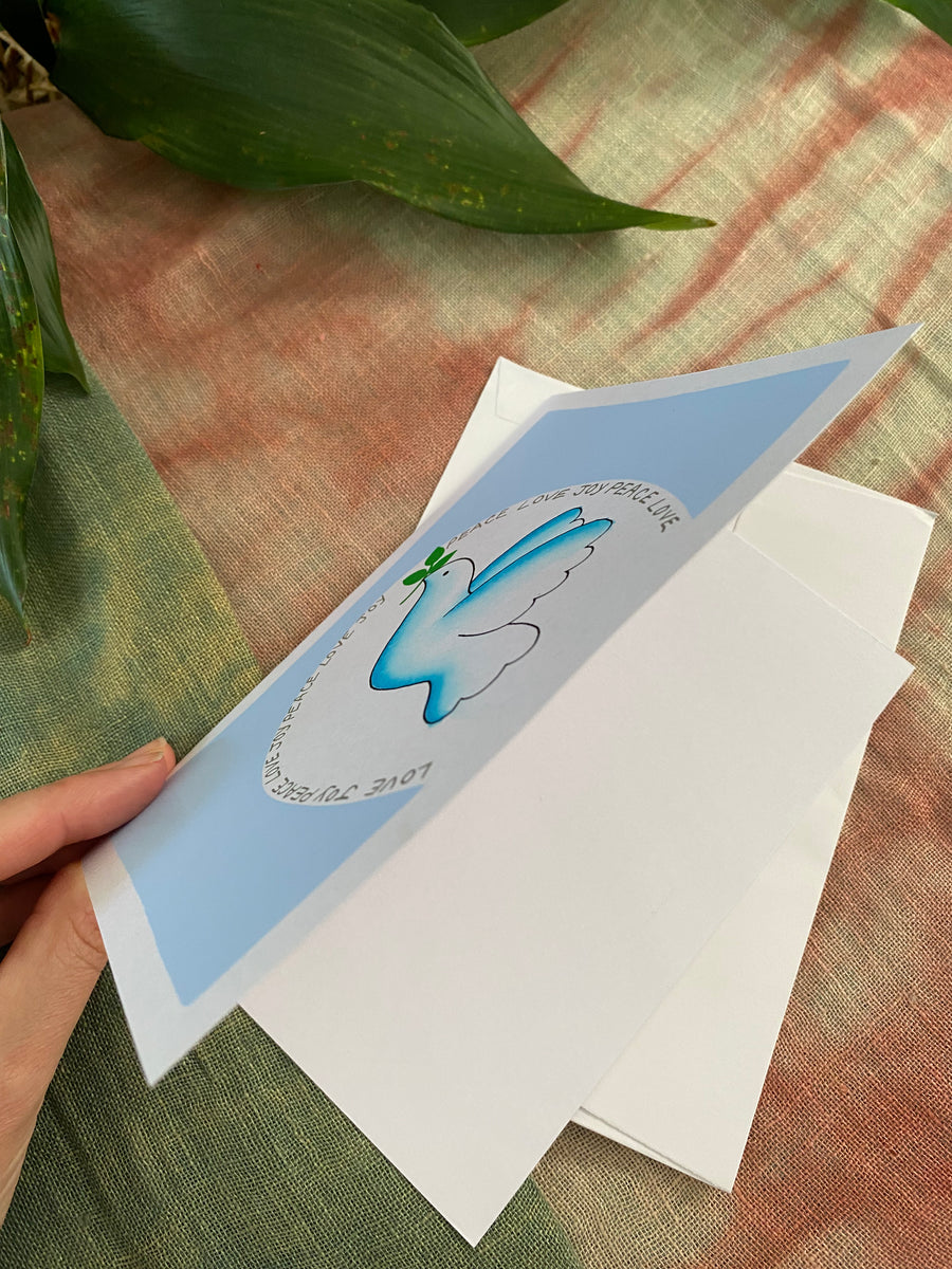 Greeting card with a dove design , with peace , love , joy written around the dove on a textured fabric background