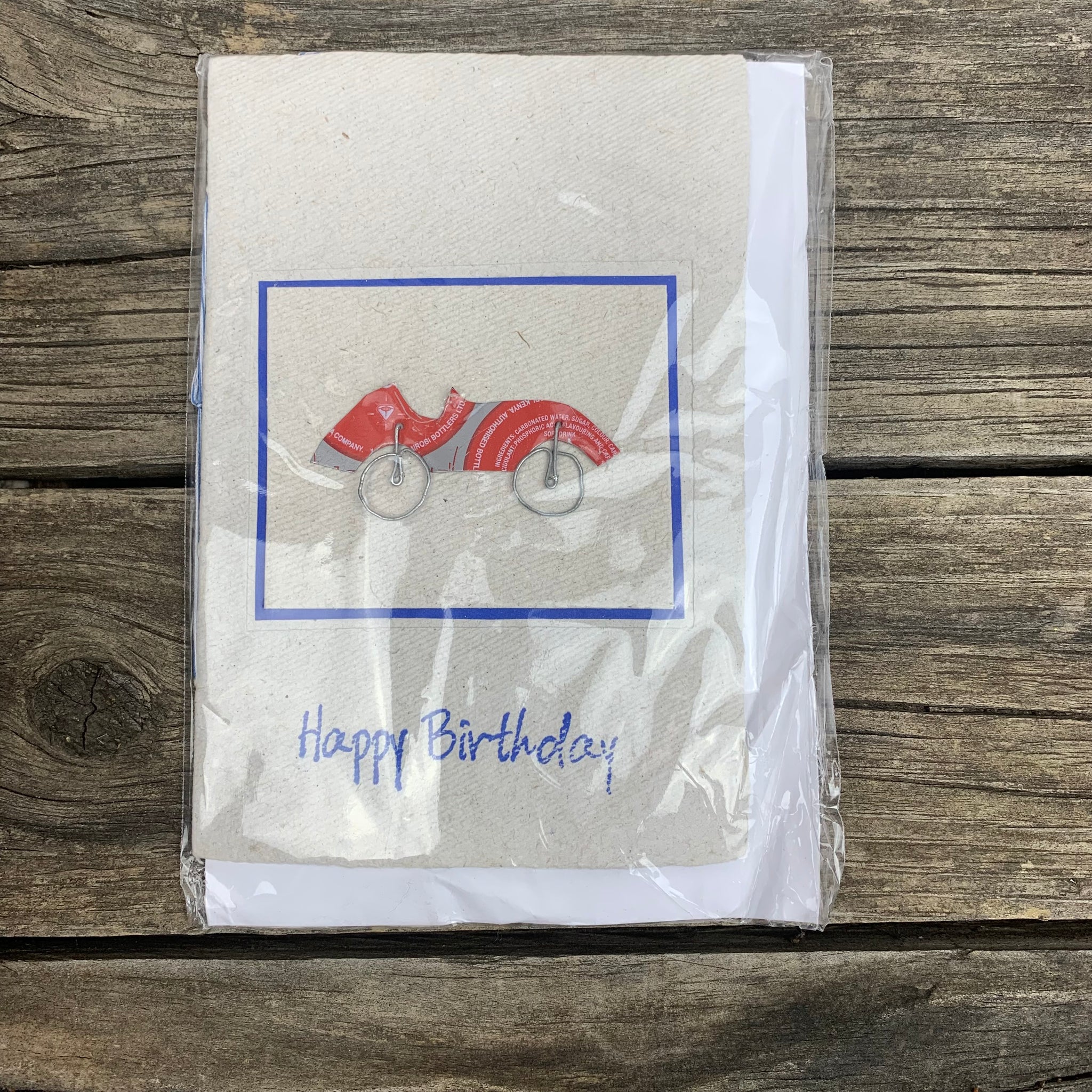White handmade paper greeting card that displays 'Happy Birthday' in blue cursive letters. In the centre of the card is a car made out of metal wire and recycled metalframed by a blue border