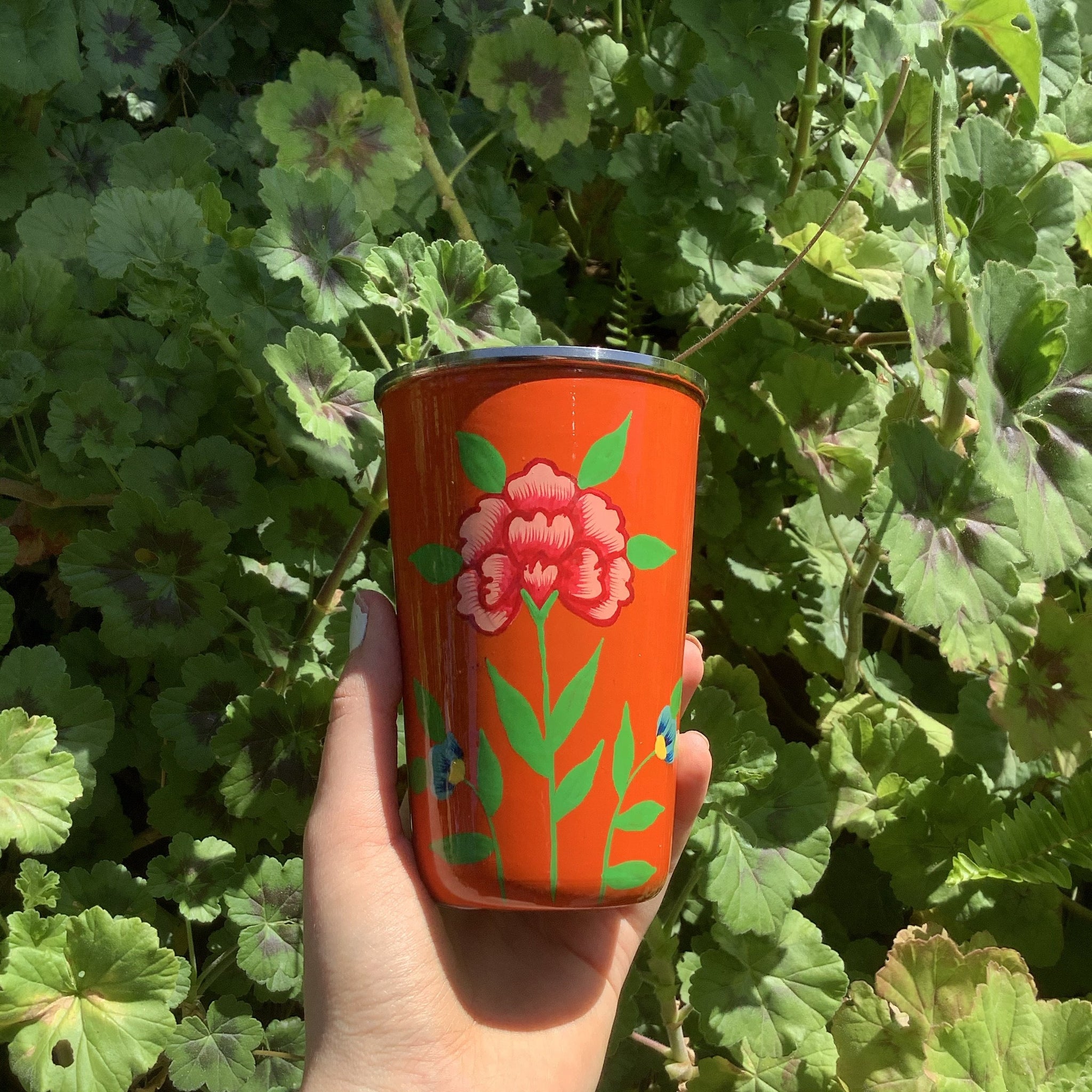 Photo of orange cup with handpainted flowers on green stem around the circumference of the exterior of the cup   