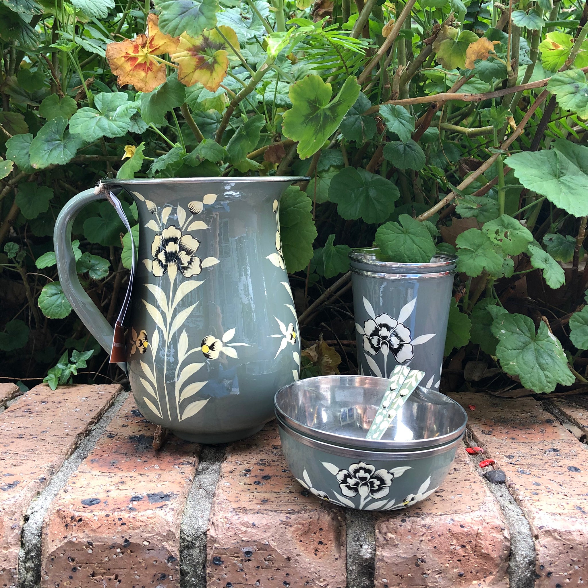 Grey Steel Set, photo includes the jug, cups, bowl and spoons. each with a grey painted background with white flowers on white stems around the circumference of each object.  